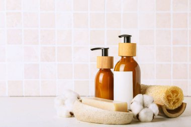 Kozmetik şişeleri, sünger ve pamuk çiçekli kompozisyon fayans duvarına karşı.