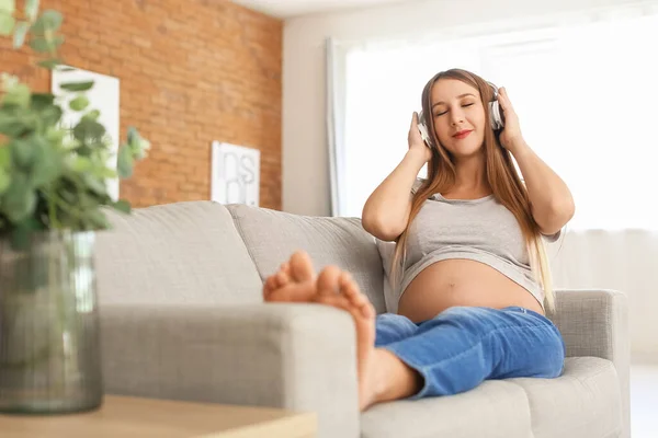 Kulaklıklı Genç Hamile Kadın Evdeki Kanepede Müzik Dinliyor — Stok fotoğraf