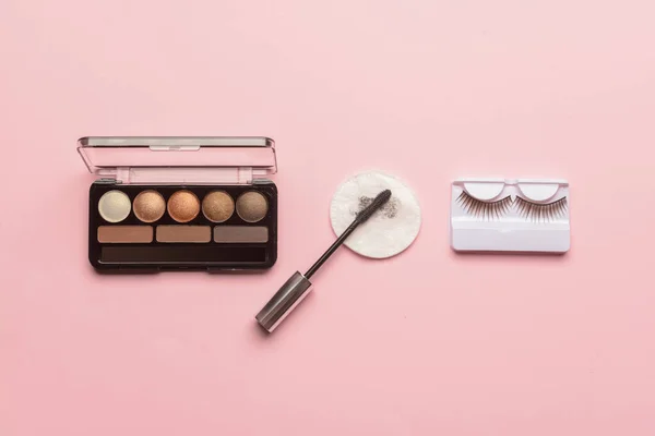 Eyeshadows, mascara, false eyelashes and used cotton pad on pink background
