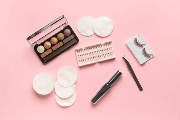 Eyeshadows, mascara, false eyelashes, tweezers and cotton pads on pink background