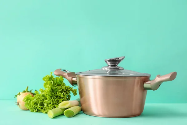 Cooking pot with vegetables on color background