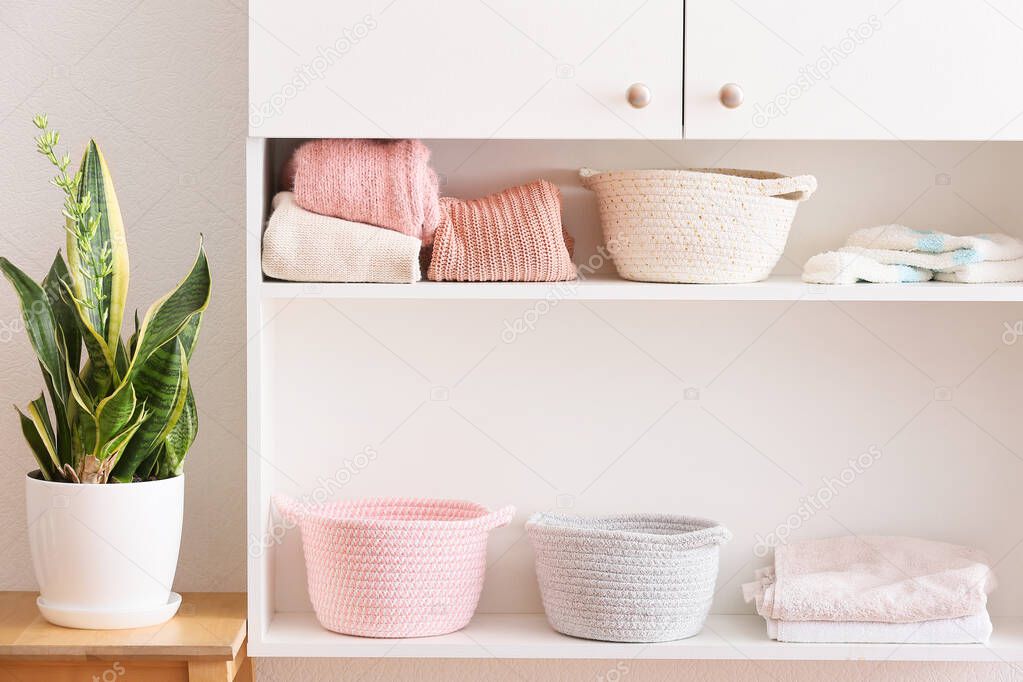 Stylish shelf unit with baskets, clean towels and clothes in room