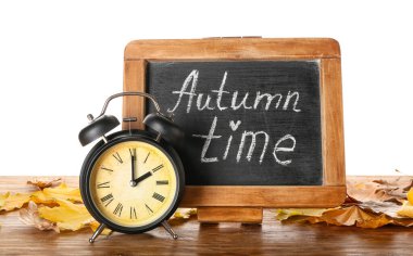 Alarm saati, karatahta ve sonbahar yaprakları beyaz arka planda. Gün ışığı kaydetme süresi bitti