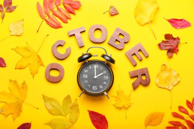 Alarm saati, ECTOBER kelimesi ve renk arkaplanda sonbahar yaprakları. Gün ışığı kaydetme süresi bitti