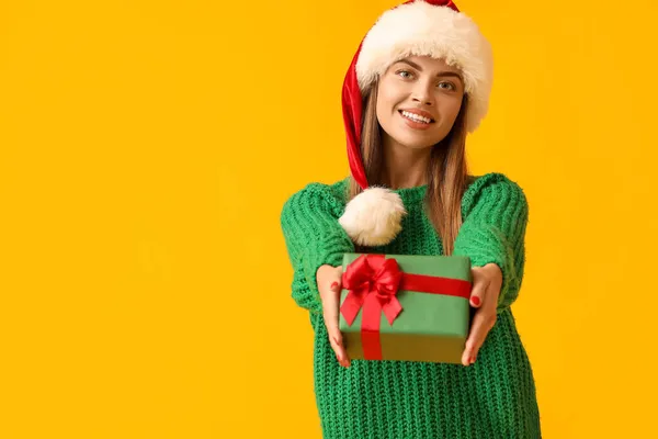 美しいです若いです女性でサンタ帽子クリスマスプレゼント上の黄色の背景 — ストック写真