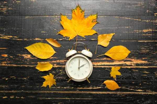 目覚まし時計と秋の黒い木製の背景に葉 昼間の節約時間終了 — ストック写真