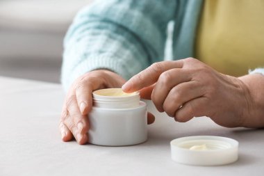 Masada ellerine makyaj kremi süren yaşlı bir kadın.