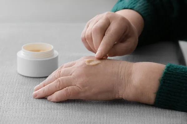 Elderly Woman Applying Cosmetic Cream Her Hands Table — Stock Photo, Image