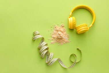 Renk arkaplanında protein tozu, mezura ve kulaklık.