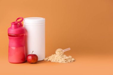 Renkli arka planda protein tozu, şişe, kavanoz ve elmayla kepçeyi ölçmek