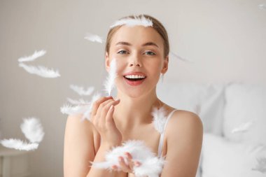 Yatak odasında yumuşak tüyleri olan güzel genç bir kadın.