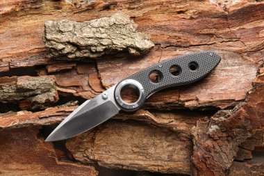 Kauçuk saplı katlanmış çakı ağaç kabuklarında yatıyor.