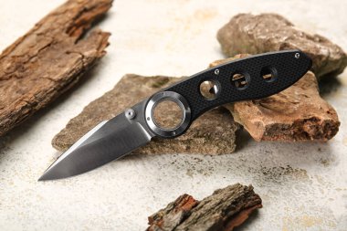 Kauçuk saplı katlanmış çakı taşların ve ağaç kabuklarının üzerinde duruyor.