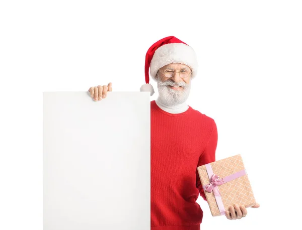 サンタクロースの帽子のスタイリッシュな大人の男性 白い背景に空白のポスターとギフトボックス — ストック写真