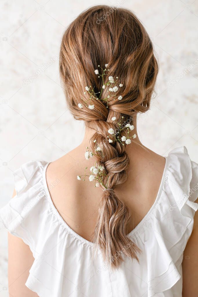 Pretty young woman with flowers in hair on light background