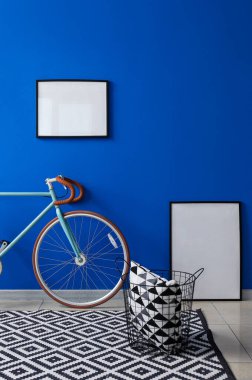 Bisiklet, boş çerçeveler ve yastıklı sepet parlak mavi duvarın yanında.
