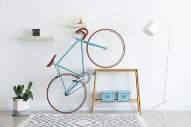 Beyaz duvarın yanında kutuları olan bisiklet, lamba ve masa.