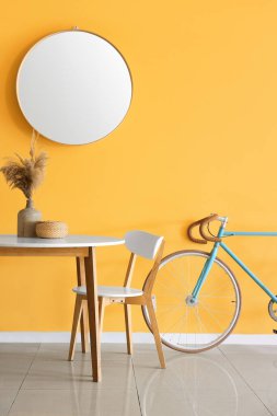 Sarı duvarın yanında vazo ve bisikletle yemek masası.