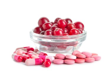 Kızılcık hapları ve beyaz arka planda bir kase dut.