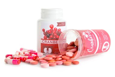 Beyaz arka planda kızılcık hapları ve kapsülleri olan şişeler.