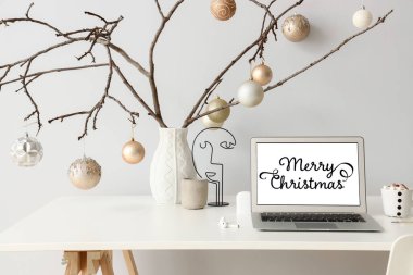 Dizüstü bilgisayarı ve ağaç dallarından Noel süslemeleri olan şenlikli bir iş yeri ve arka planda farklı toplar.