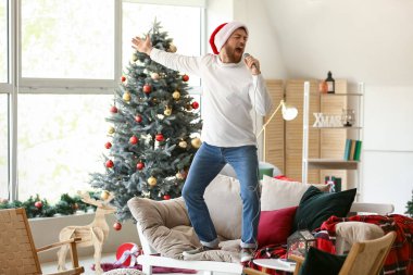 Genç adam Noel arifesinde evde mikrofonla şarkı söylüyor.