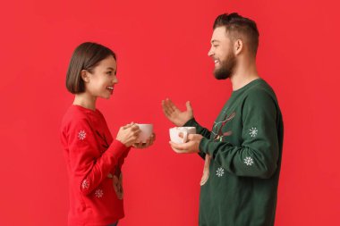 Şık Noel elbiseli genç bir çift ve renkli arka planda sıcak çikolata bardakları var.
