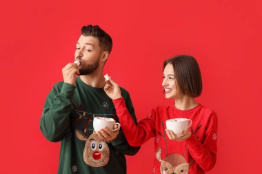 Şık Noel elbiseli genç bir çift ve renkli arka planda sıcak çikolata bardakları var.
