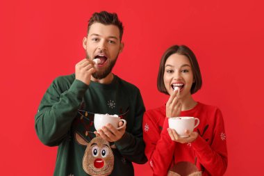 Şık Noel elbiseli genç bir çift ve renkli arka planda sıcak çikolata bardakları var.