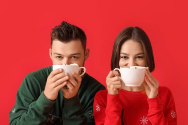 Şık Noel elbiseli genç bir çift ve renkli arka planda sıcak çikolata bardakları var.