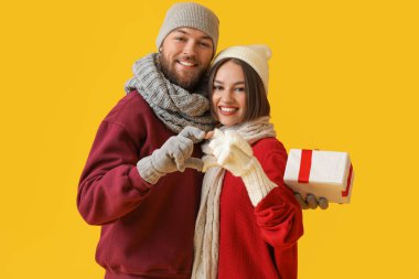 Şık kış kıyafetleri içinde mutlu genç bir çift ve renkli arka planda bir Noel hediyesi.