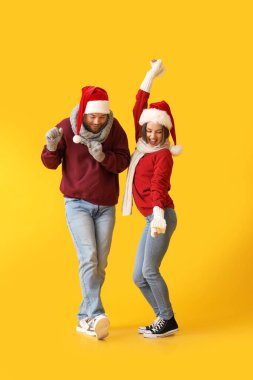 Şık kış kıyafetleri içinde dans eden genç bir çift ve renkli arka planda Noel Baba şapkaları