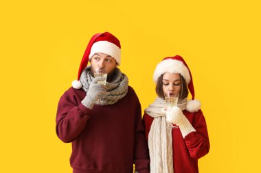 Noel Baba şapkalı genç bir çift ve renkli arka planda şampanya kadehleri var.