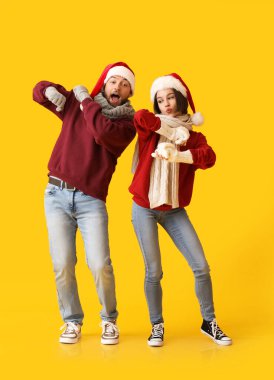 Şık kış kıyafetleri içinde dans eden genç bir çift ve renkli arka planda Noel Baba şapkaları