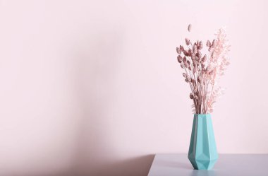 Işık duvarının yanındaki masada güzel kurumuş çiçekli vazo.