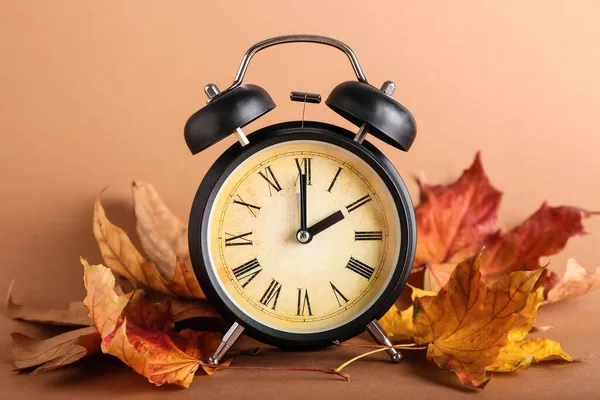 目覚まし時計と秋の茶色の背景に葉 昼間の節約時間終了 — ストック写真