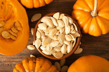 Doğal kabak tohumları ve ahşap arka planda taze sebzelerle dolu bir kase.