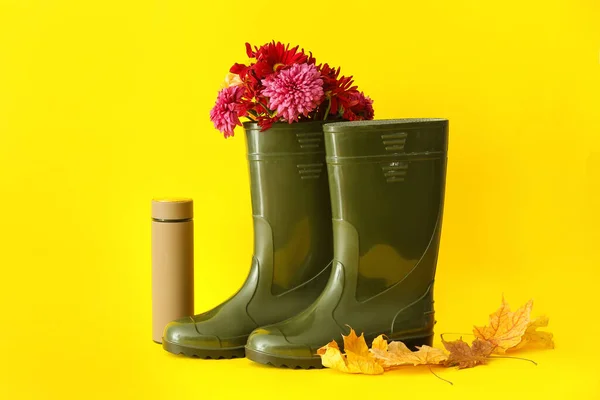 Buty Gumowe Kwiatami Termosem Opadłymi Liśćmi Żółtym Tle — Zdjęcie stockowe