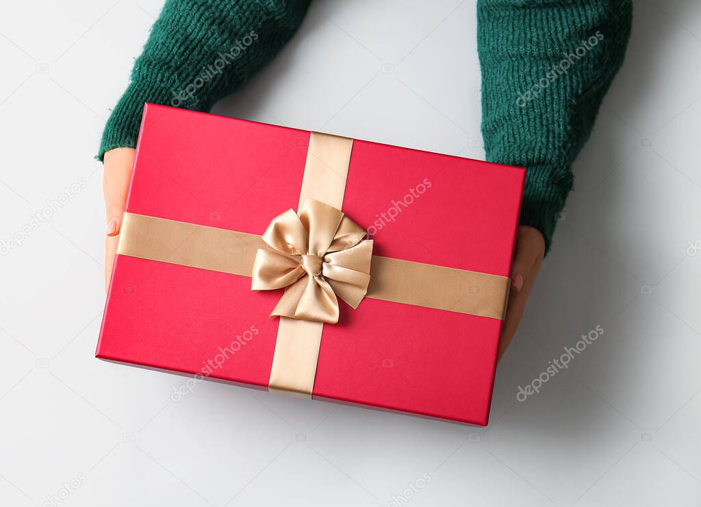 Female hands with Christmas gift box on light background