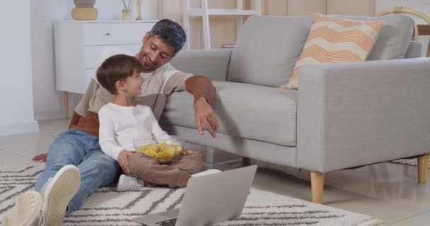 Mann Und Sein Kleiner Sohn Mit Laptop Essen Chips Hause — Stockvideo