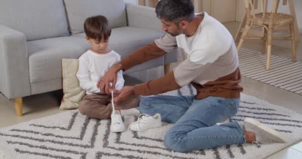 家で靴ひもを結ぶように息子に教える男 — ストック動画
