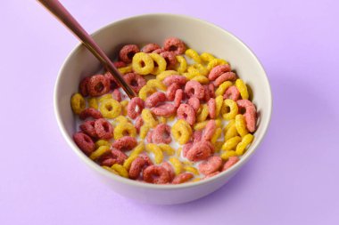 Kıtır kıtır mısır gevreği halkaları ve renkli sütle dolu bir kase.