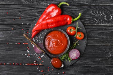 İçinde organik domates sosu ve koyu ahşap arka planda malzemeler olan bir kase.