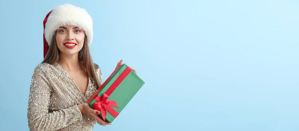 美しいです若いです女性でサンタ帽子とととともにクリスマスプレゼント上の青の背景にテキストのためのスペース — ストック写真