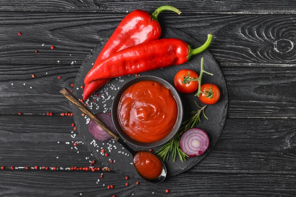 İçinde organik domates sosu ve koyu ahşap arka planda malzemeler olan bir kase.