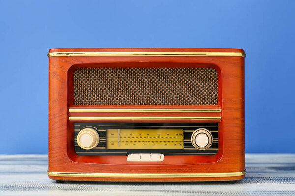 Retro radio receiver on table against color background