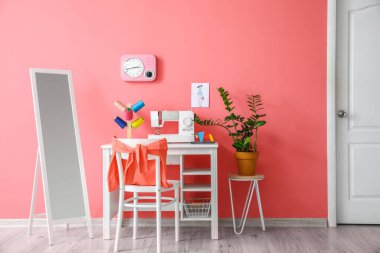 Modern terzi işyeri, dikiş makinesi ve pembe duvarın yanındaki iplikler.