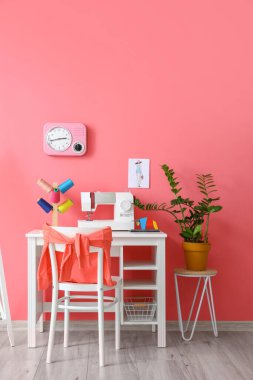 Modern terzi işyeri, dikiş makinesi ve pembe duvarın yanındaki iplikler.
