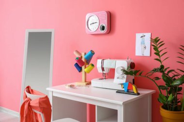 Modern terzi işyeri, dikiş makinesi ve pembe duvarın yanındaki iplikler.