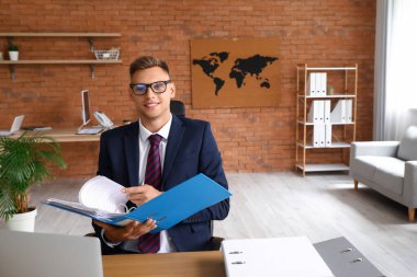 Ofiste belgelerle çalışan genç adam.